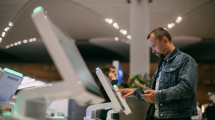 Eine Person steht an einem elektronischen Check-in-Schalter am Flughafen und checkt für den Flug ein.