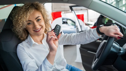 Lächelnde Person sitzt am Steuer eines PKWs und hält Autoschlüssel in der Hand