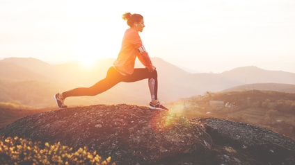 Person dehnt sich im Sonnenuntergang auf Fels stehend