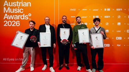 Sieger und Gratulanten beim AMADEUS 2026 – Tonstudiopreis BEST SOUND: Neun Personen vor Hintergrund in Orange