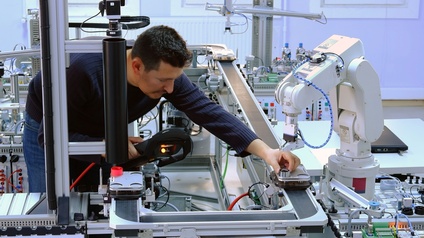 Ein Mechatroniker richtet einen Roboterarm zur Bearbeitung eines Metallproduktes auf dem Fließband ein