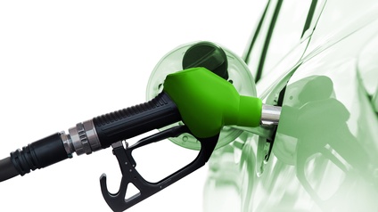 Detailansicht eines grünschwarzen Benzinzapfhahnes der in Tanköffnung eines Autos im Ausschnitt steckt und sich darin spiegelt vor weißem Hintergrund