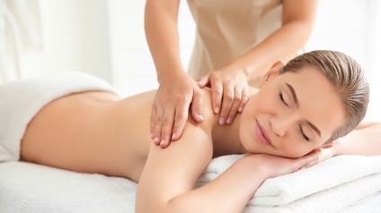 Eine Person liegt auf einem Tisch mit nacktem Oberkörper. Die untere Körperhälfte ist mit einem Handtuch bedeckt. Das Gesicht der Person ist zur Kamera gedreht. Zwei Hände einer anderen Person liegen auf dem Rücken der ersten Person und sind in Bewegung