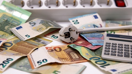 Verschiedene Eurogeldscheine durcheinander liegend, darauf Taschenrechner und Stromverteiler platziert