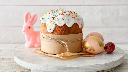Osterkuchen mit Glasur und bunten Streuseln auf einem Teller, im Hintergrund steht ein rosa Hase und lugt beim Kuchen hervor