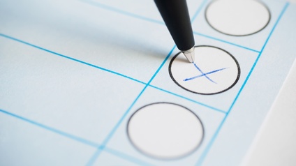 Auf einem Papier wird mit einem Kugelschreiber ein Kreuz gesetzt, um bei einer Wahl die Stimme abzugeben