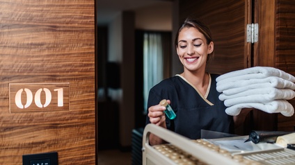 Freudige Person in Arbeitskleidung bei der Reinigung eines Hotelzimmers