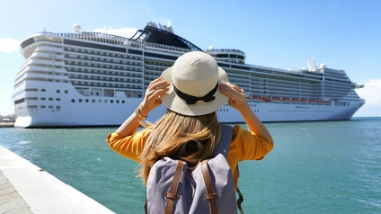 Junge Touristin mit Rucksack steht vor einem Kreuzfahrtschiff