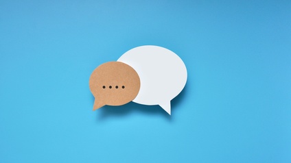Auf blauem Hintergrund sind zwei Sprechblasen. Die linke Sprechblase sind braun. In ihr sind vier schwarze Punkte. Die rechte Sprechblase ist weiß und leer