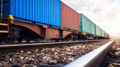 Güterwaggons stehen auf einem Bahngleis und sind mit verschiedenfarbigen Containern beladen