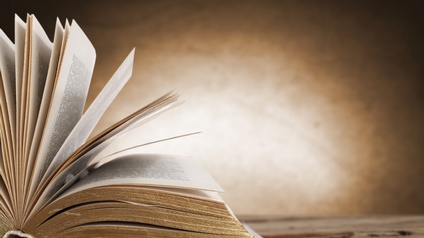 Ein aufgeklapptes Buch auf einer Holzoberfläche vor braunem Hintergrund.