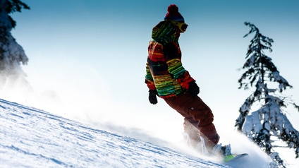Person in winterlicher Kleidung fährt mit einem Snowboard im Schnee