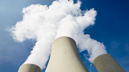 Drei Atomreaktortürme, aus denen Rauch austreten vor blauem Himmel