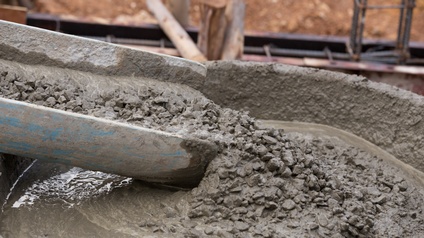 Aus einer Rutsche fließt flüssiger Beton in einen Behälter