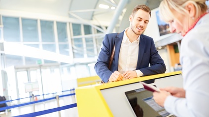Lächelnde Person beugt sich über gelben Schalter zu Person verschwommen im Vordergrund, die Pass kontrolliert