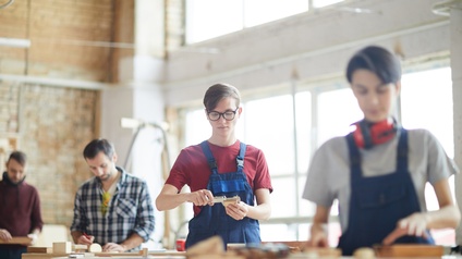 Mehrere Personen in Arbeitsoveralls an Werkbänken stehend und Holz bearbeitend