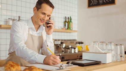 Person mit Schürze hinter Bar stehend macht auf Clipboard Notizen