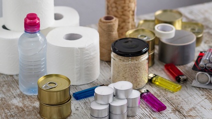 Sammelsurium unterschiedlicher Gegenstände eines Survival-Kits: Dosen, Flaschen, Teelichter, Feuerzeuge, Batterien, Toilettenpapier