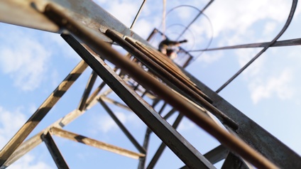 Ansicht von unten eines Metallmastens, oben verschwommen Person unter wolkenverhangenem Himmel erkennbar