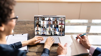 Personen blicken auf Laptopbildschirm mit mehreren online Teilnehmenden bei Meeting