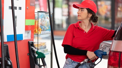 Person in roter Arbeitskleidung tankt ein Auto und blickt dabei auf die Tankanzeige