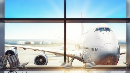 Ein Flugzeug steht auf einer Landebahn. Davor ist der Wartebereich eines Flughafens