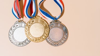 Nahaufnahme dreier Medaille dicht nebeneinander von links nach rechts in den Metallen Silber, Gold und Bronze