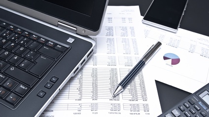 Büroalltag mit Laptop, Smartphone, Taschenrechner, Kugelschreiber und Finanzdokumenten