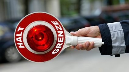 Hand hält ein rot-weißes Warnschild mit Halt Grenze