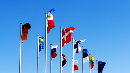 Verschiedene Fahnenmasten mit unterschiedlichen Flaggen Europas wehen im Wind bei einem blauen Himmel