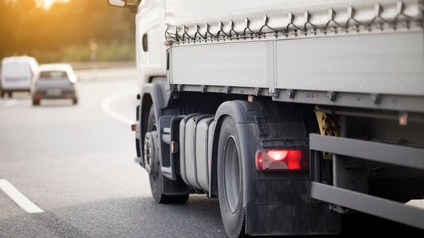 Nahaufnahme der linken Seite eines Lastkraftwagens, der auf einer Straße fährt. Vor dem LKW fahren zwei Autos.