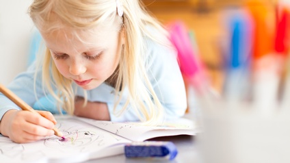 Kind über Buch gebeugt malend