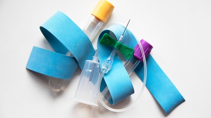 Verschiedene Medizinprodukte wie Katheter und Ampullen nebeneinander drapiert, blaues Muskelband durchgewoben