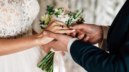 Nahaufnahme von einem Brautpaar mit Brautkleid, Brautstrauß und Anzug während des Ansteckens eines Ringes