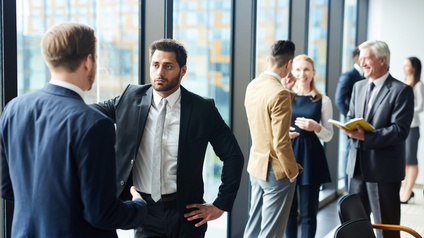 In einem großen Raum mit einer großen Fensterfront stehen viele verschiedene Personen in Kleingruppen und unterhalten sich