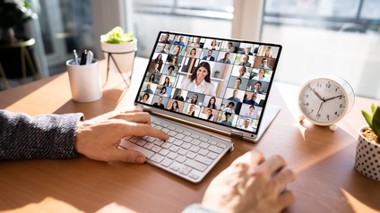 Teilnahme an einer virtuellen Konferenz über ein Tablett mit Tastatur, das auf einem Schreibtisch platziert ist, daneben steht ein Wecker, mehrere kleine Zierpflanzen sowie ein Stiftehalter
