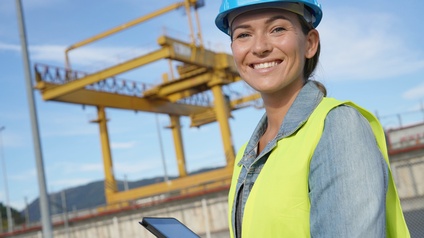 Porträt einer Person mit Helm, Sicherheitsweste und einem Tablet in der Hand, die auf einer Baustelle steht
