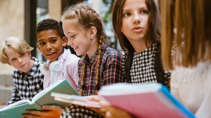 Fünf Kinder sitzen nebeneinander und halten Bücher in den Händen