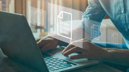 Eine Person sitzt an einem Tisch an einem aufgeklappten Laptop. Über dem Laptop sind als Grafik vier weiße Zettel nebeneinander. Auf jedem Zettel sind Linien und Häkchen. Die Person tippt auf dem Laptop
