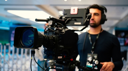 Person mit Headset und Ausweis bedient eine Filmkamera