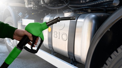 Detailansicht eines grünschwarzen Treibstoffzapfhahnes von Hand gehalten, im Hintergrund Tank eine Gefährtes mit der Aufschrift Bio