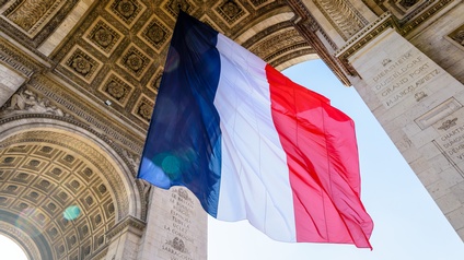 Die französische Flagge weht im Wind, im Hintergrund das Gewölbe des Triumphbogens