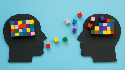 Illustration zweier Köpfe, im Bereich des Gehirns sind bunte Würfel platziert, vor dem Mund eines Kopfes sind weitere bunte Würfel in Richtung des anderen Kopfes verstreut.