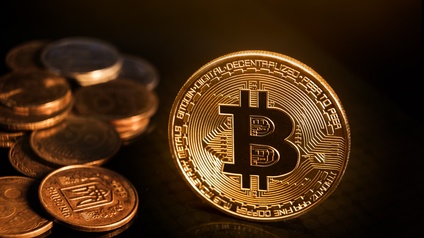 Stehende goldenen Münze geprägt mit Bitcoin-Zeichen, nebenliegend weitere Münzen