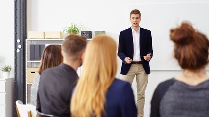 Person in Businesskleidung spricht vor Publikum in einem Besprechungsraum