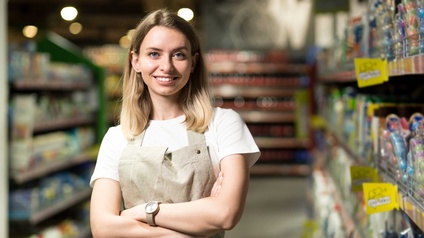 Eine junge Frau steht mit verschränkten Armen in einem Supermarkt