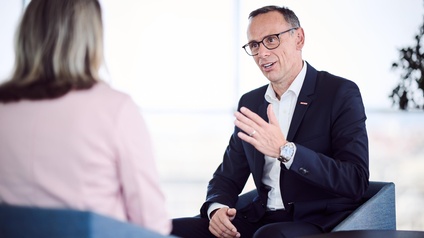 Generalsekretär Mag. Jochen Danninger sitzend im Gespräch mit einer Person in rosa Oberteil