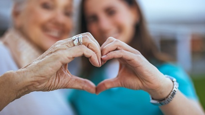 Eine ältere und eine jüngere Frau formen gemeinsam mit den Händen ein Herz.