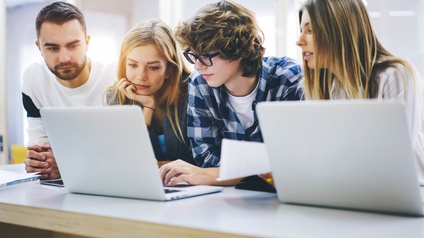 Vier junge Personen blicken auf aufgeklapptes Notebook.