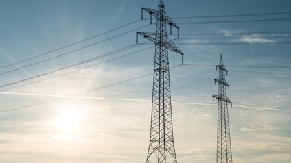 Strommasten unter leicht bewölktem aber blauen sonnigen Himmel